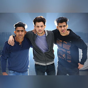 Three Young Men Standing Together in Casual Streetwear Against a Blue Sky HD phone wallpaper