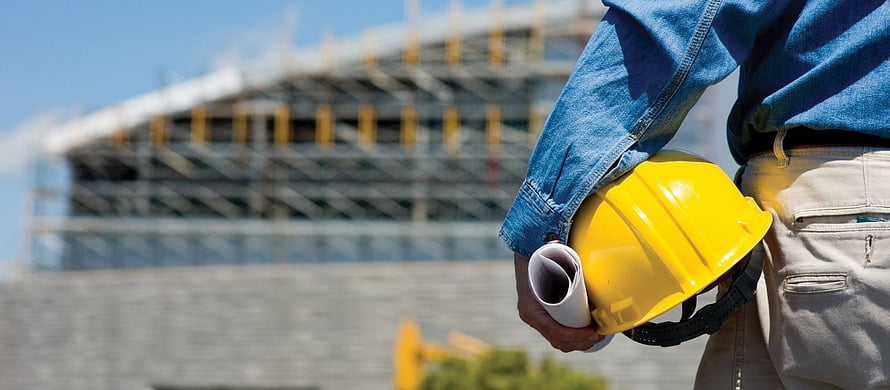 Construction worker holding yellow hard hat and blueprints in front of building site HD wallpaper