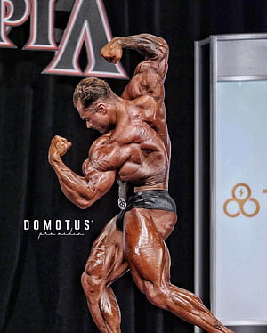 Chris Bumstead Bodybuilder Stage Pose with Defined Musculature and Oiled Skin HD phone wallpaper