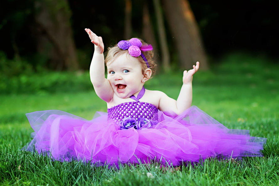 Smiling baby girl in a purple tulle dress sitting on green grass with arms raised HD wallpaper