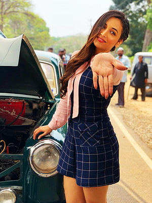 Srinidhi Shetty posing in a navy checkered dress beside a vintage car with an open hood HD phone wallpaper