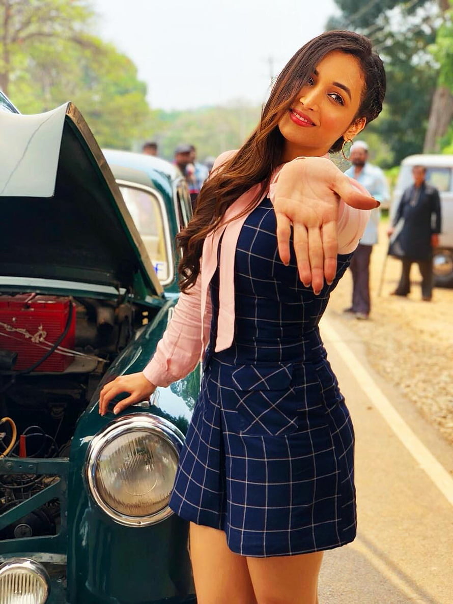 Srinidhi Shetty posing in a navy checkered dress beside a vintage car with an open hood HD phone wallpaper