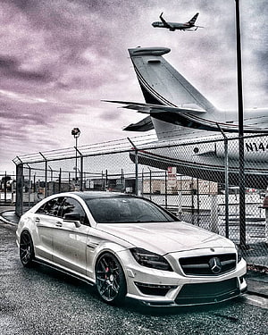 Silver Mercedes-Benz CLS 63 AMG parked at an airport with a private jet in the background HD phone wallpaper