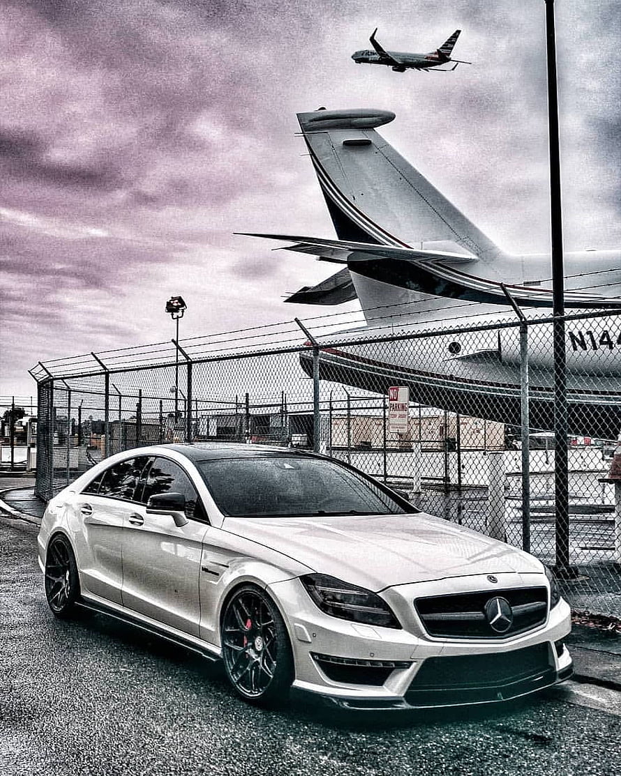 Silver Mercedes-Benz CLS 63 AMG parked at an airport with a private jet in the background HD phone wallpaper
