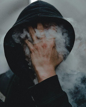 Moody Portrait of a Hooded Figure with Hand Over Face Surrounded by Thick White Smoke HD phone wallpaper