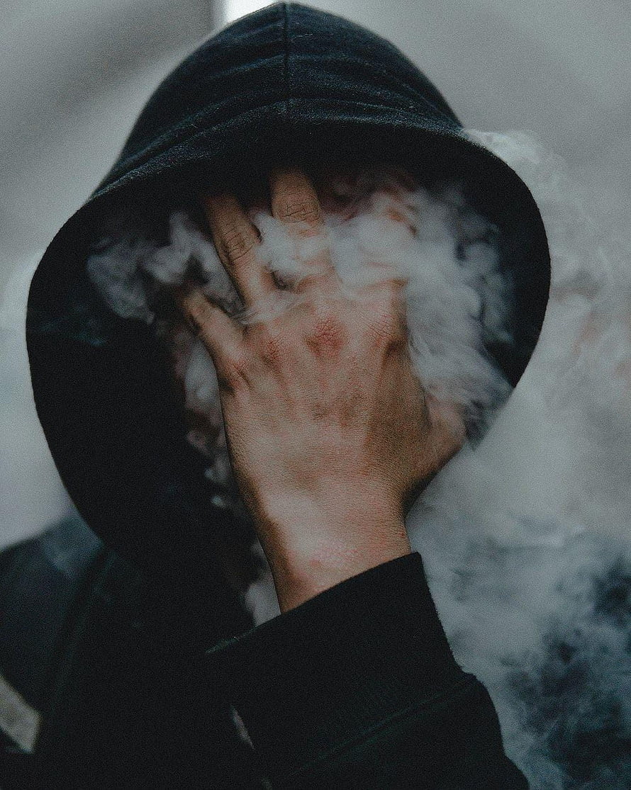 Moody Portrait of a Hooded Figure with Hand Over Face Surrounded by Thick White Smoke HD phone wallpaper