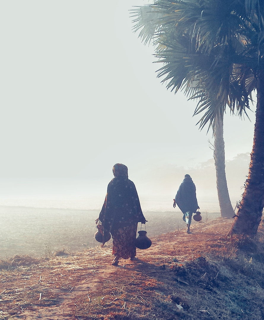 Two women carrying water pots walk along a rural path in Bangladesh during winter morning HD phone wallpaper