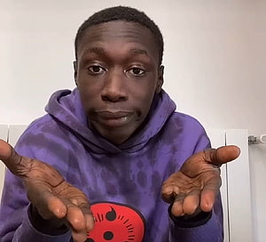 Khaby Lame in purple hoodie with expressive open hands gesture HD wallpaper