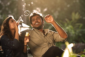 Neram Movie Still: Man and Woman Blowing Bubbles in Golden Sunlight HD wallpaper