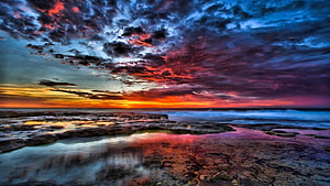 Dramatic Coastal Sunset with Fiery Clouds and Rocky Shoreline Reflections HD wallpaper