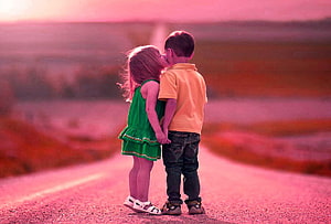 Two young children sharing a tender kiss on a rural road at sunset HD wallpaper