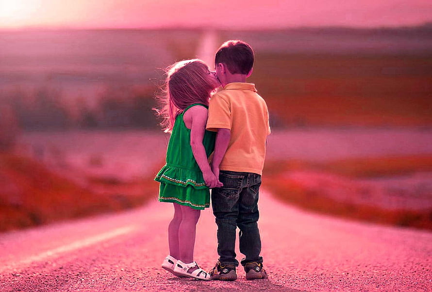 Two young children sharing a tender kiss on a rural road at sunset HD wallpaper