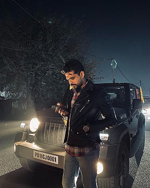 Arjan Dhillon posing in a black leather jacket beside a Maruti Gypsy at night HD phone wallpaper