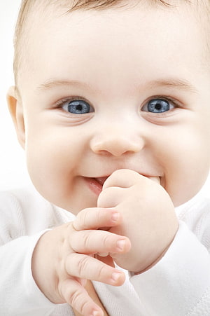 Close-up portrait of a smiling baby boy with bright blue eyes and a hand near his mouth HD phone wallpaper
