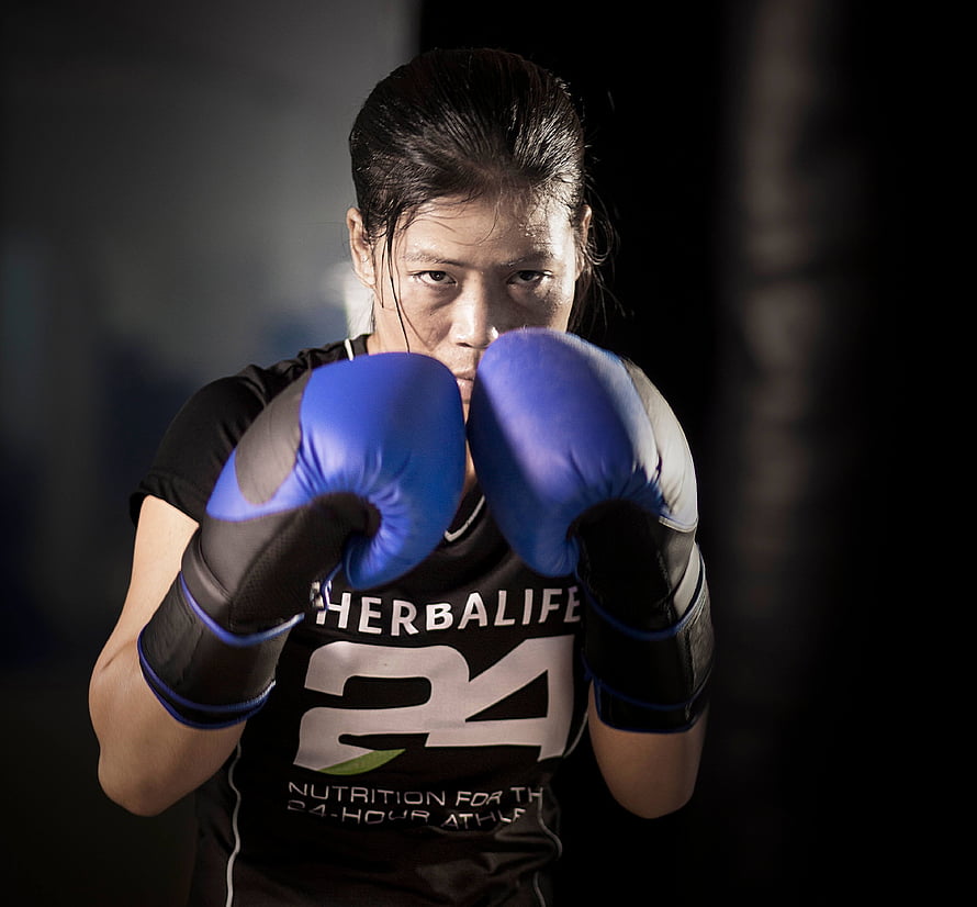 Mary Kom in a focused boxing stance wearing blue gloves and a Herbalife training shirt HD wallpaper