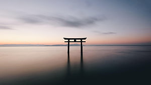 Silhouette of a Japanese Torii Gate Standing in Calm Ocean Water at Dusk HD wallpaper
