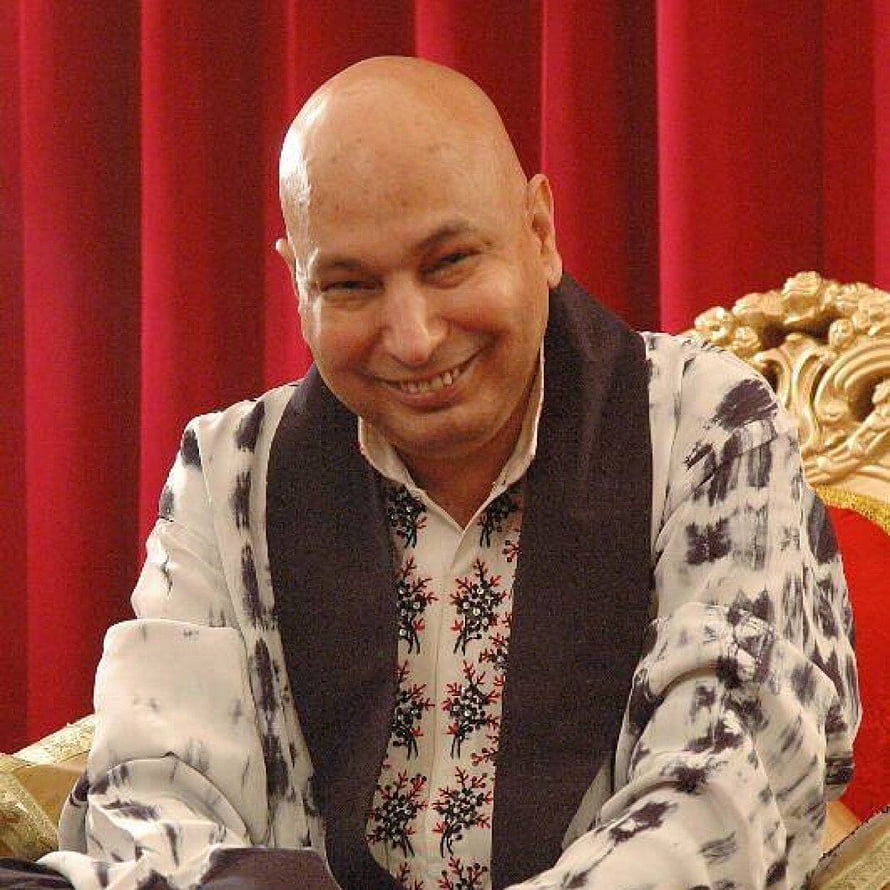 Portrait of a smiling bald man in a patterned shirt and dark vest seated before a red curtain HD phone wallpaper