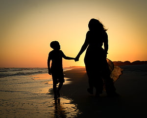 Mother and son silhouette walking hand in hand along the shoreline at sunset HD wallpaper