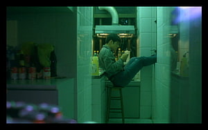 Chungking Express cinematic still of a man sitting on a stool in a green-lit kitchen HD wallpaper