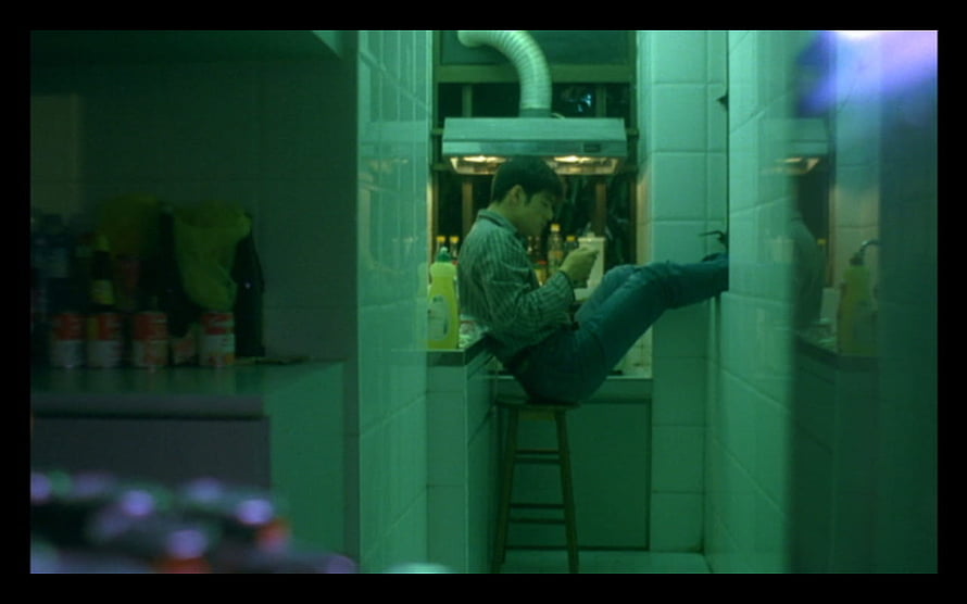 Chungking Express cinematic still of a man sitting on a stool in a green-lit kitchen HD wallpaper