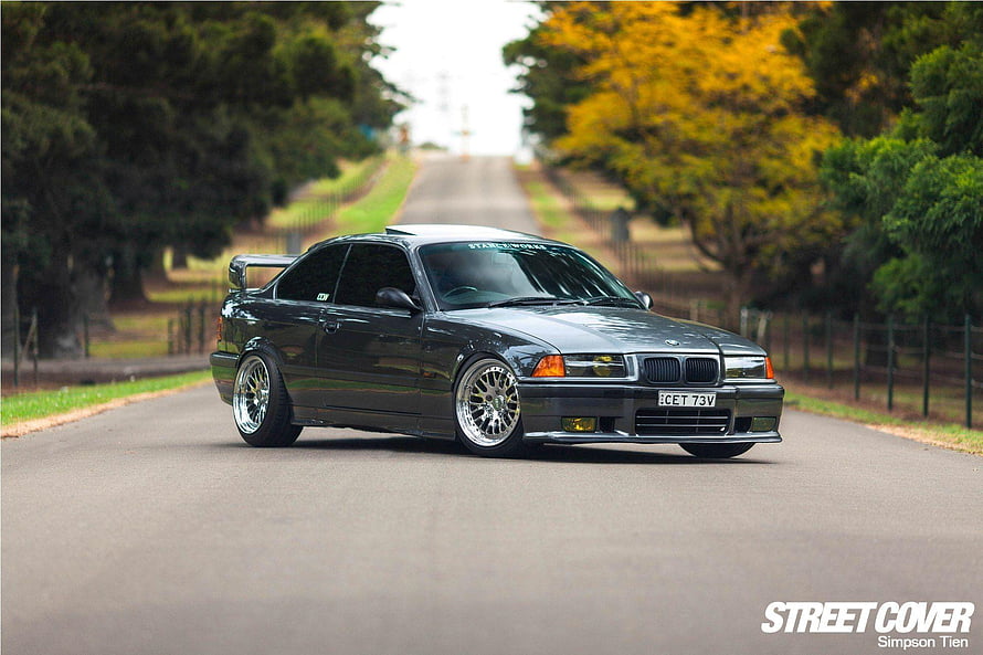 Black BMW M3 E36 Coupe with Widebody Kit and Deep Dish Wheels on a Tree-Lined Road HD wallpaper