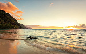 Golden sunset over a calm tropical beach with lush green cliffs and gentle ocean waves HD wallpaper