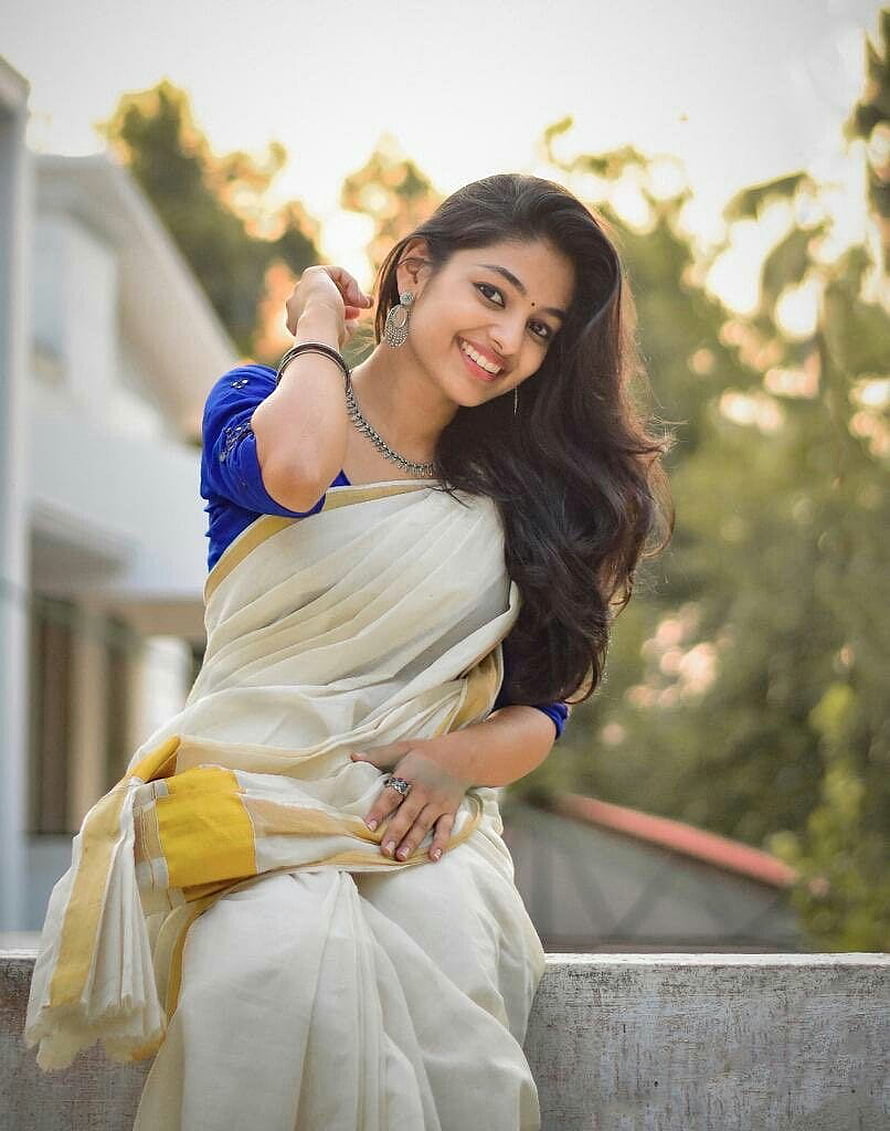 Aleena Shaji in a cream and gold saree with a blue blouse, smiling outdoors HD phone wallpaper