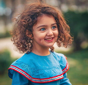 Portrait of a smiling young girl with curly brown hair and blue eyes wearing a blue dress HD wallpaper