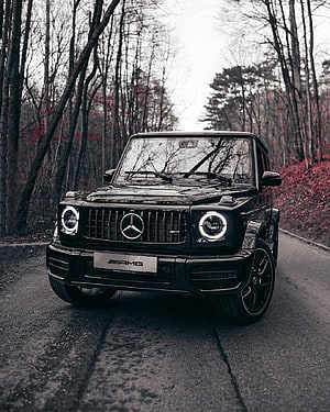 Black Mercedes-Benz G-Class AMG parked on a forest road with circular LED headlights HD phone wallpaper
