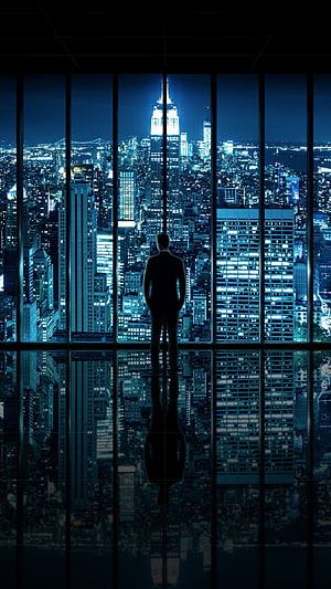 Silhouette of a businessman overlooking a glowing city skyline at night from a high-rise window HD phone wallpaper