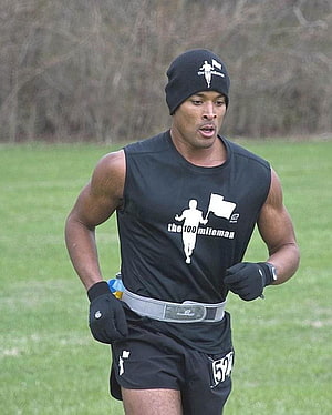 David Goggins Running in Black Sleeveless Shirt and Beanie on a Grassy Field HD phone wallpaper