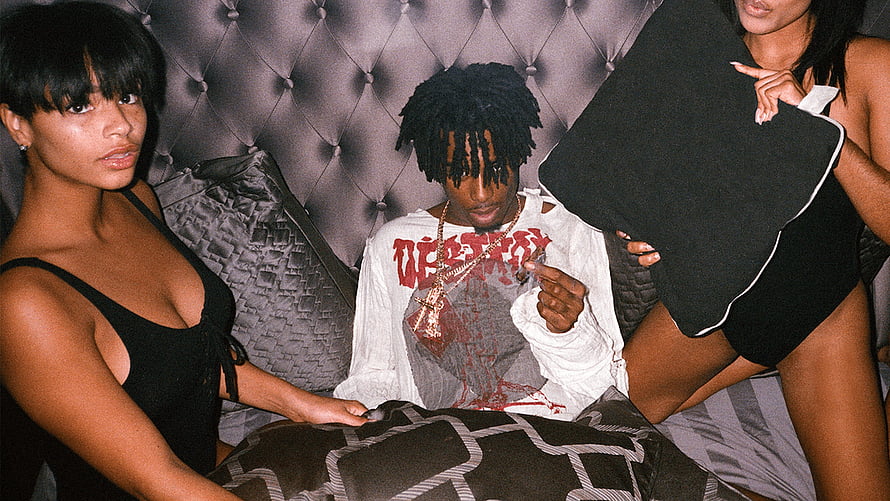 Playboi Carti in distressed white shirt with gold chain on tufted bed with two women HD wallpaper