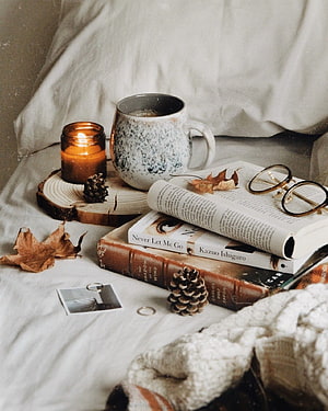 Cozy Autumn Reading Nook with Candle, Books, and Pinecones on a Bed HD phone wallpaper
