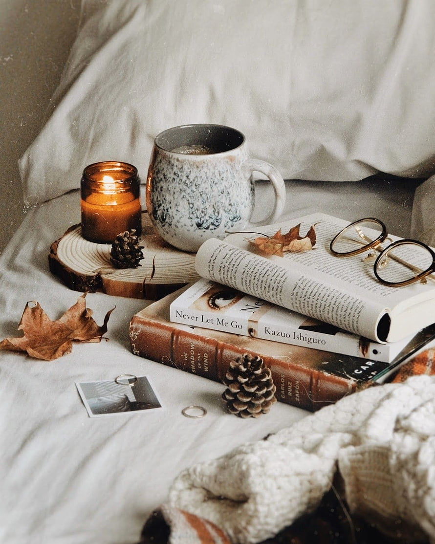 Cozy Autumn Reading Nook with Candle, Books, and Pinecones on a Bed HD phone wallpaper