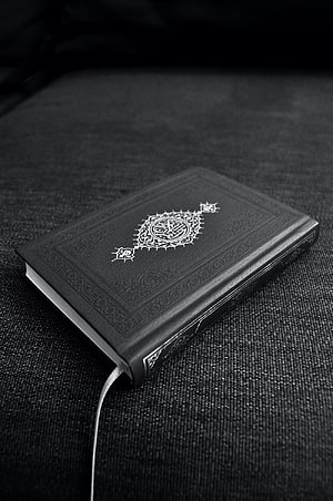Black Quran with ornate gold calligraphy on dark textured fabric background HD phone wallpaper