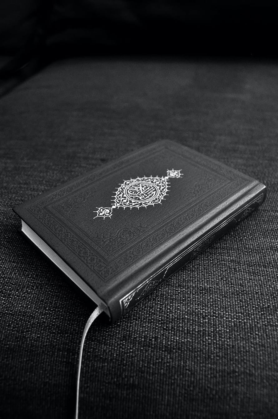Black Quran with ornate gold calligraphy on dark textured fabric background HD phone wallpaper