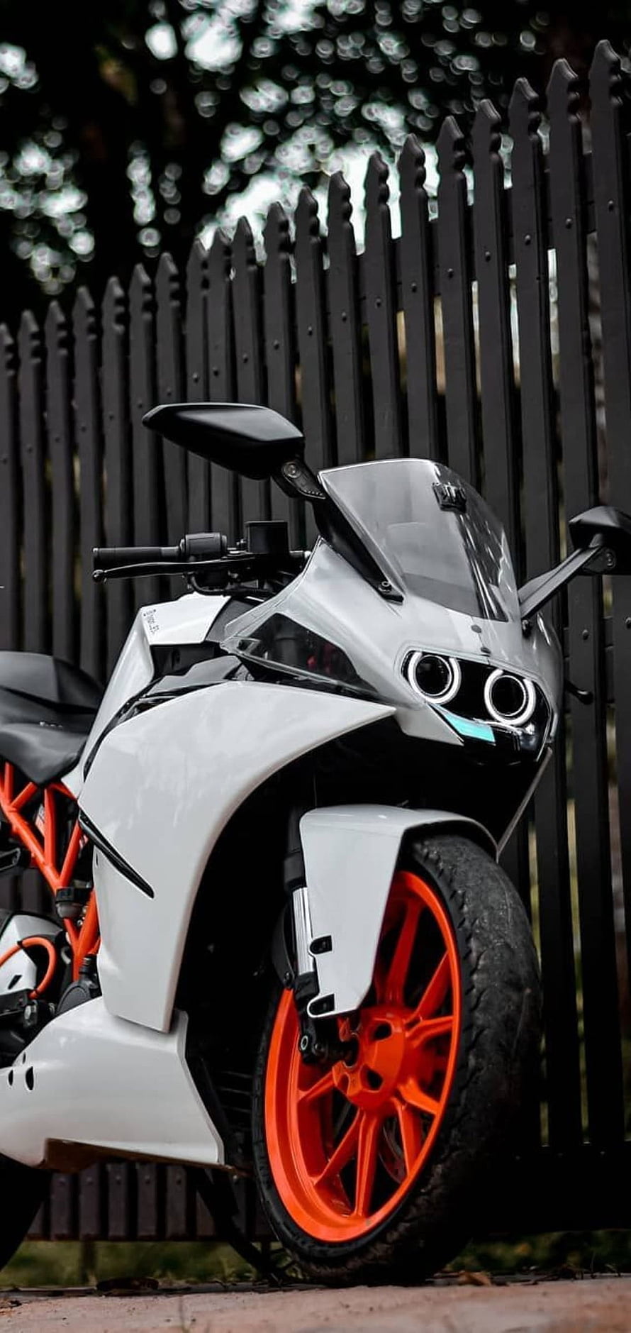 White KTM RC 390 sport motorcycle with orange wheels parked against a black metal fence HD phone wallpaper