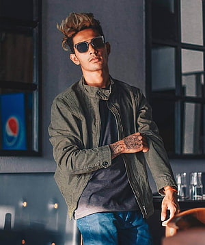 Danish Zehen in olive bomber jacket and sunglasses with visible hand tattoos in moody urban setting HD phone wallpaper