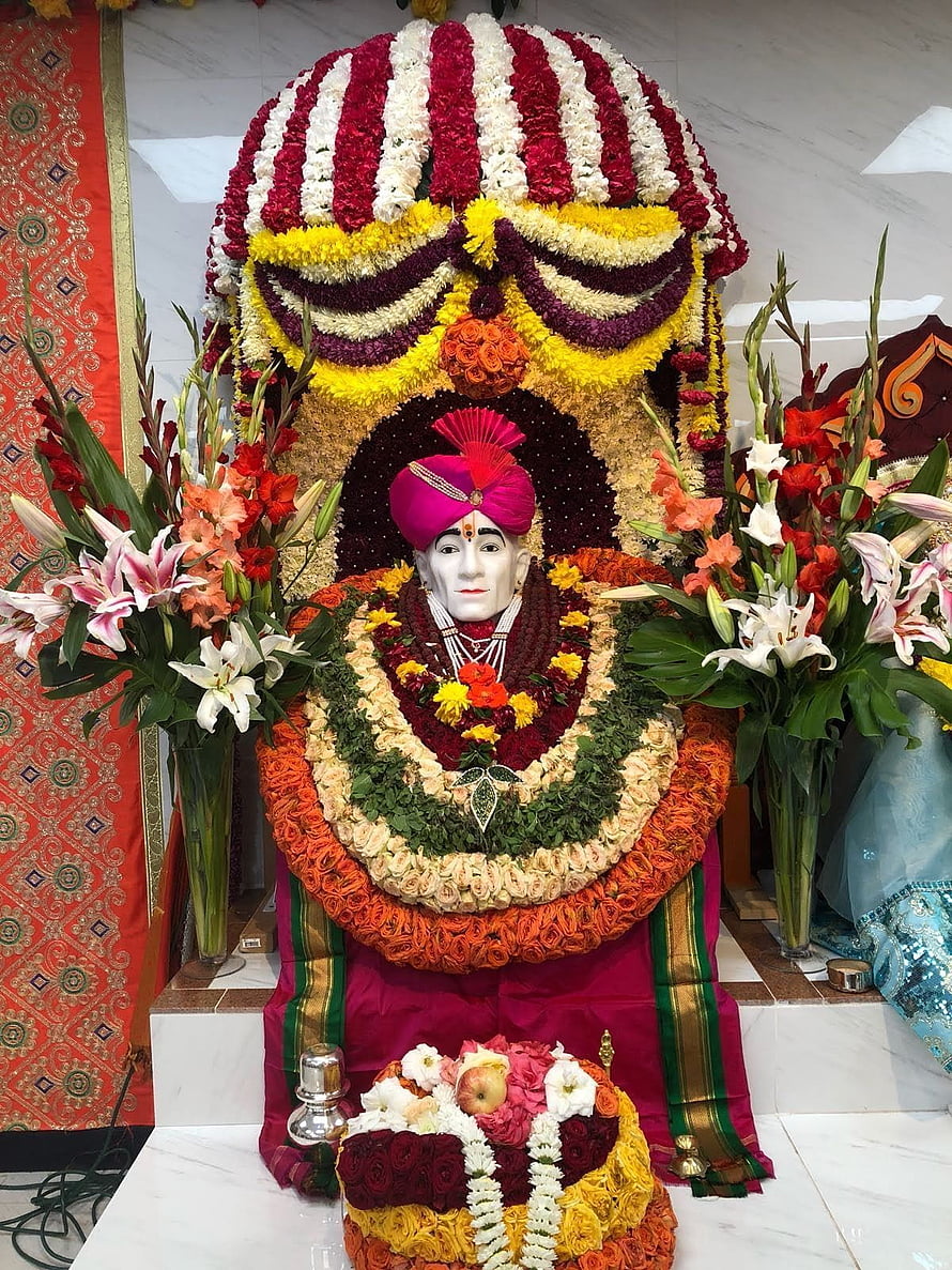 Gajanan Maharaj deity adorned in vibrant floral garlands and traditional pink turban HD phone wallpaper