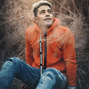 Danish Zehen in orange hoodie and distressed denim sitting in dry grass HD phone wallpaper