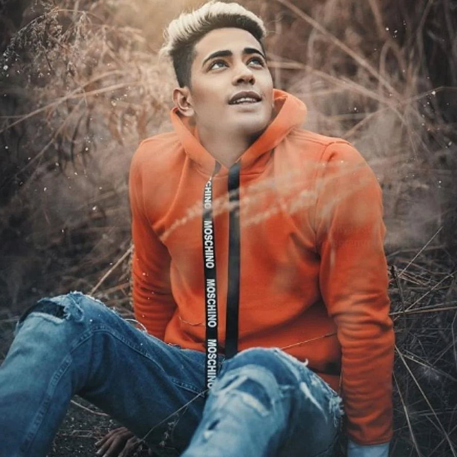 Danish Zehen in orange hoodie and distressed denim sitting in dry grass HD phone wallpaper