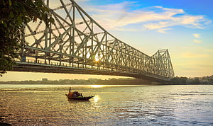 Howrah Bridge in Kolkata at Golden Hour with a Traditional Boat on the Hooghly River HD wallpaper