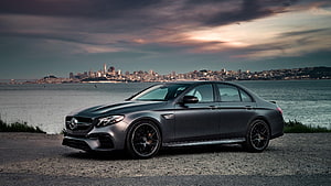 Mercedes-Benz E63 S AMG Sedan Parked on Gravel Shoreline with City Skyline at Dusk HD wallpaper