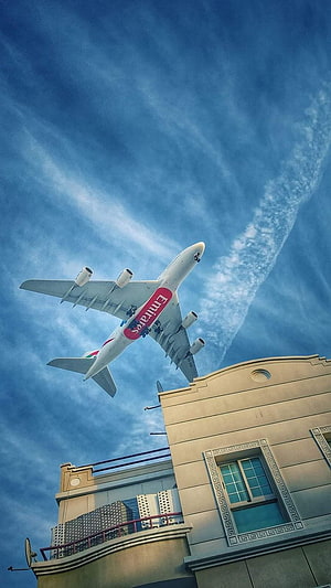 Emirates Airliner Ascending Over Urban Rooftop Against Blue Sky HD phone wallpaper