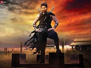 Allu Arjun warrior character standing on battlements with dual swords against fiery sunset sky HD wallpaper