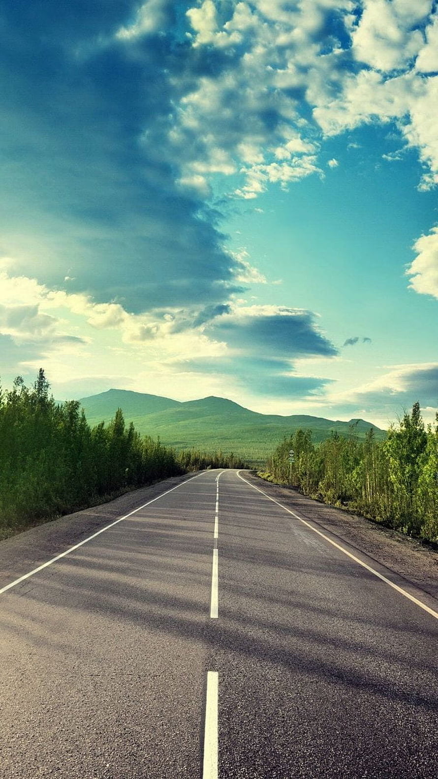 Empty Highway Stretching Toward Green Hills Under a Dramatic Cloudy Sky HD phone wallpaper