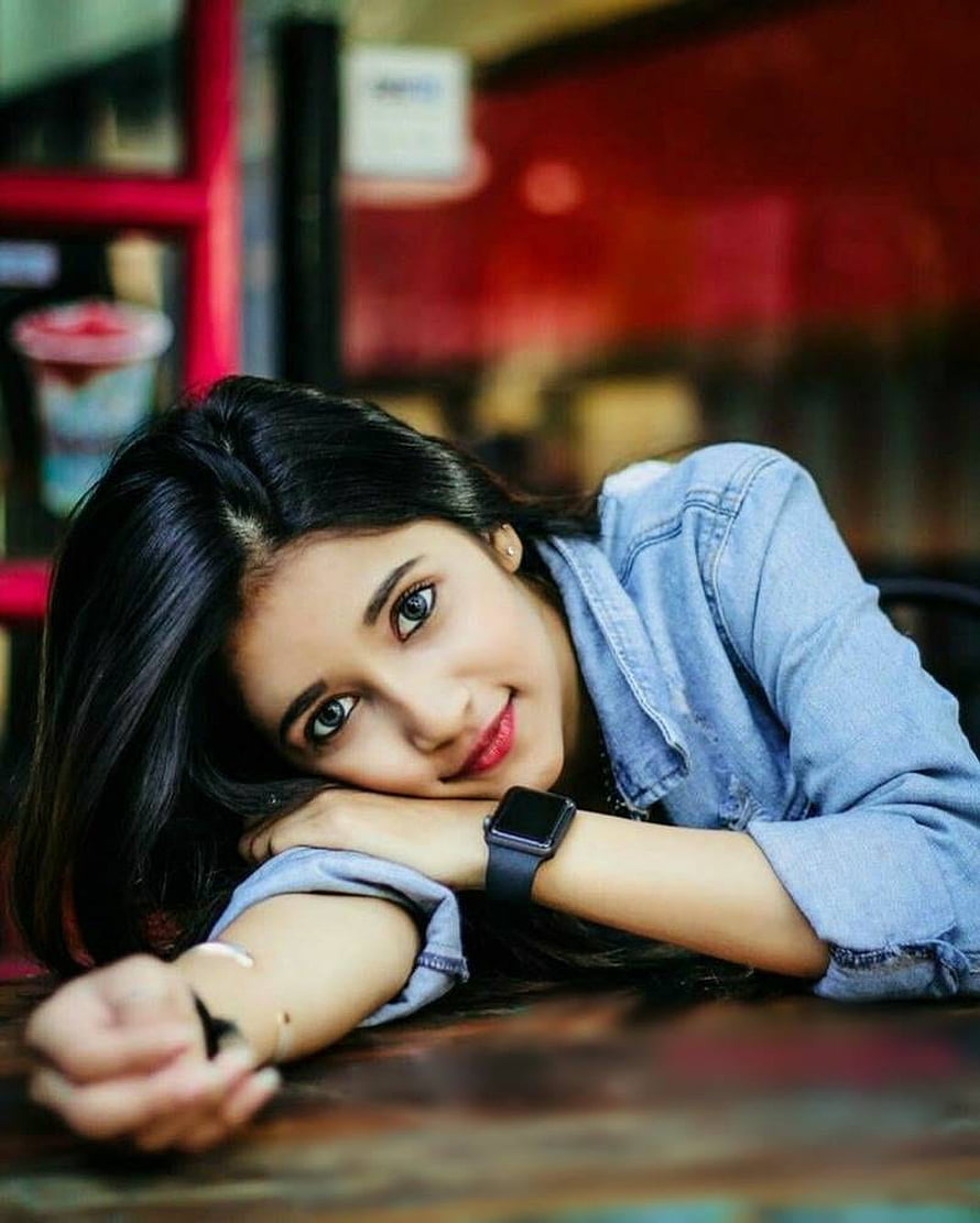 Young woman in denim shirt resting head on arms at a wooden table in a cafe HD phone wallpaper