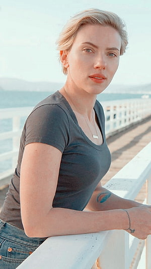 Scarlett Johansson in a grey t-shirt leaning on a white railing with a coastal backdrop HD phone wallpaper