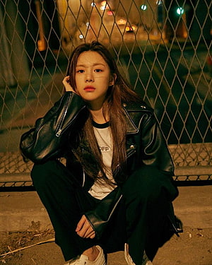 Goo Yoon Jung in a black leather jacket crouching against a chain-link fence at night HD phone wallpaper