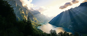 Sunlit Alpine Valley with a Serene Lake and Dramatic Mountain Peaks HD wallpaper